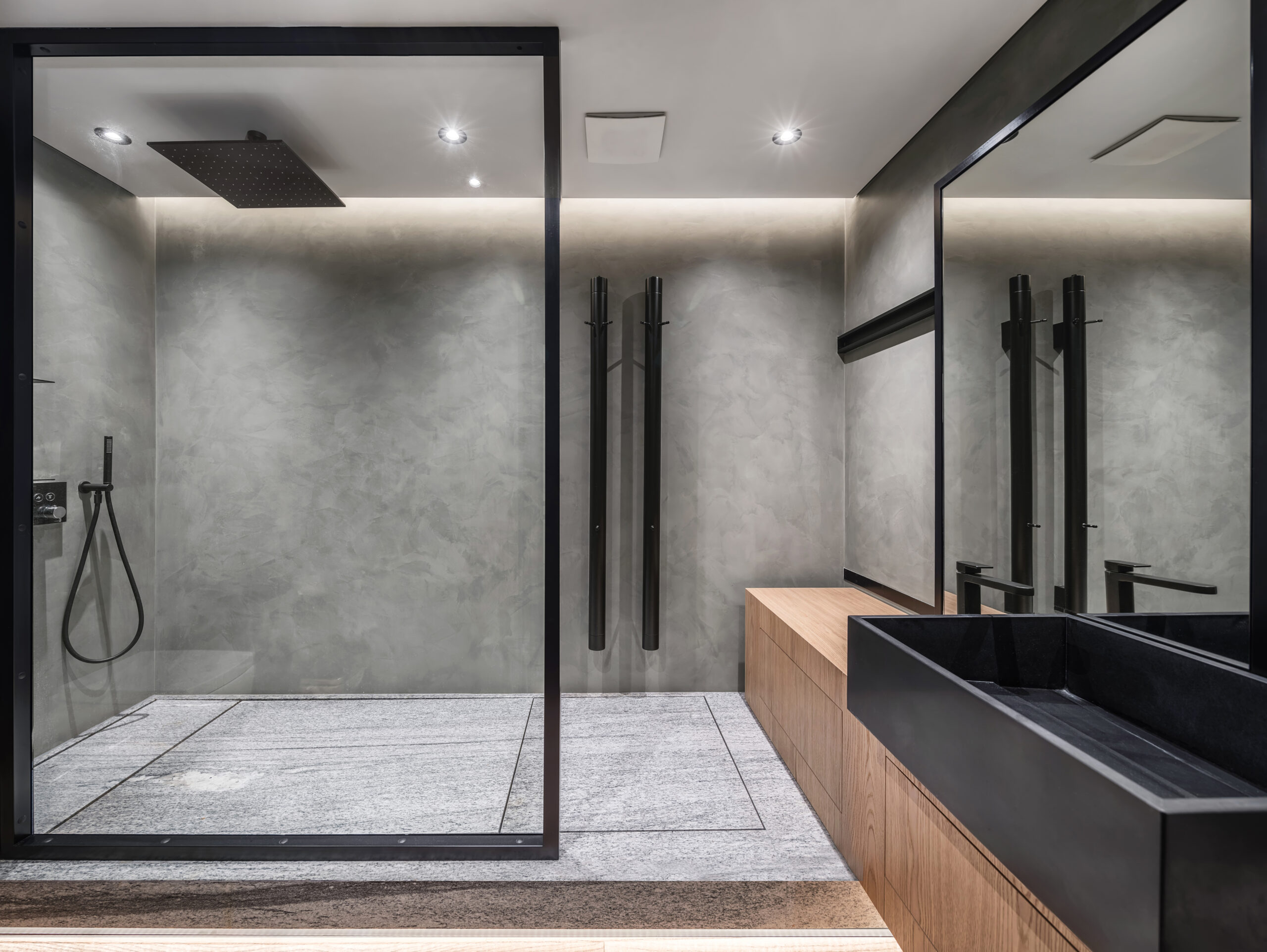 Modern bathroom featuring a glass shower, sleek fixtures, and minimalist design elements. Gray walls and wooden accents create a contemporary aesthetic.