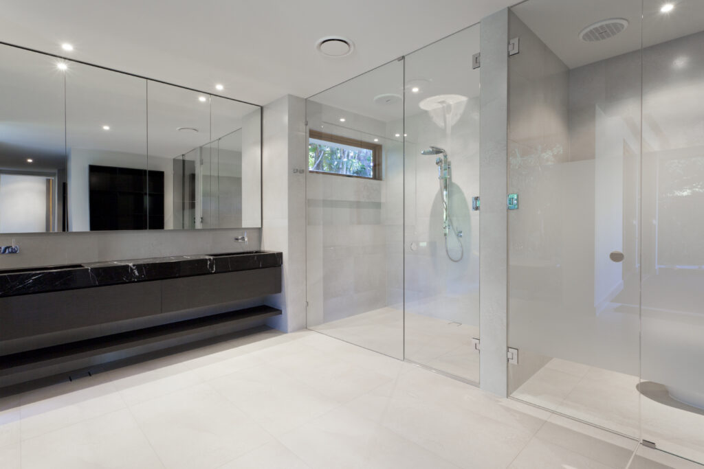 Modern bathroom featuring a sleek black vanity, large mirrors, and a glass-enclosed shower. Brightly lit with neutral tones and minimalist design.