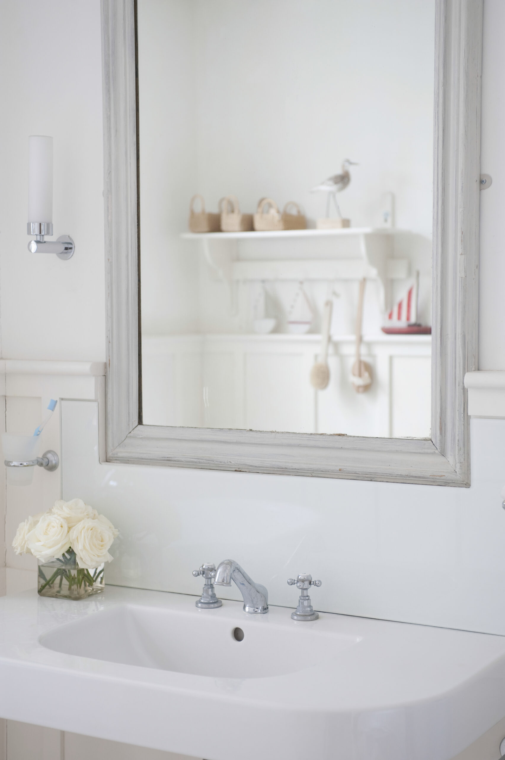 Stylish bathroom sink with chrome faucets and a glass vase of white roses, reflecting a simple, serene decor with a mirror in the background.