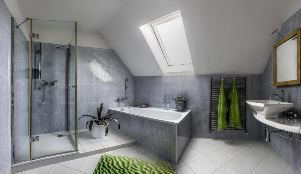 Modern bathroom with glass shower, freestanding tub, and green accents. Features sleek tile design, natural light from skylight, and potted plants.