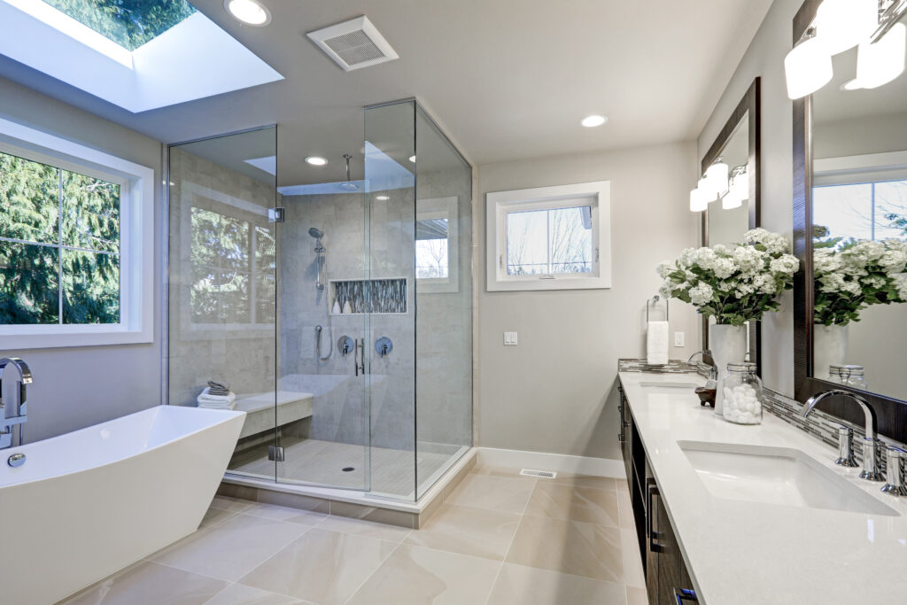 Modern bathroom featuring a glass shower, freestanding bathtub, dual sinks, and ample natural light from skylights and windows. Elegant design details enhance the space.